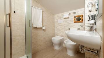 A modern bathroom with a glass shower enclosure, a white sink, and two toilets.