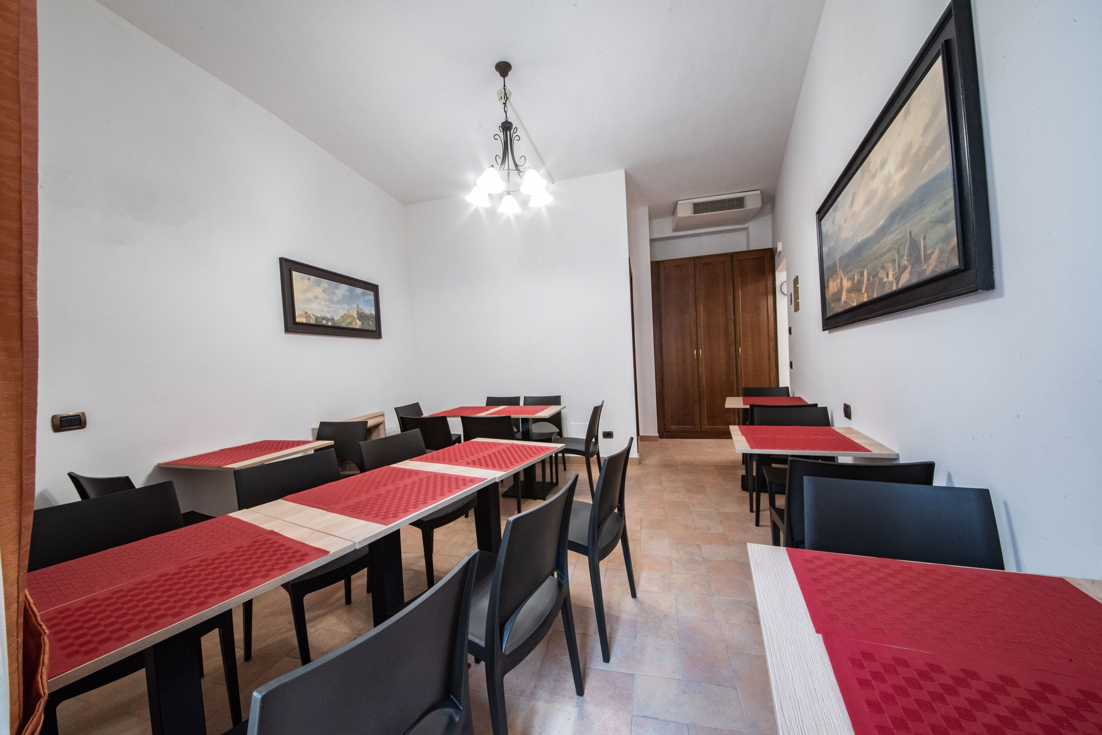 Zona pranzo con tavoli e sedie, un lampadario e un quadro appeso al muro.