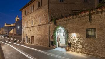 Un edificio de piedra con una entrada bien iluminada, una torre de campanas al fondo y una calle pavimentada al frente.