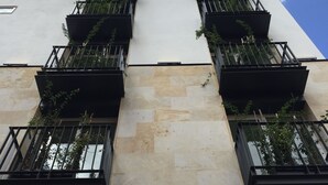 Un immeuble à la façade en pierre beige, doté de nombreux balcons avec des garde-corps noirs.
