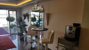 A hotel lobby with a reception desk, two bar stools, a coffee machine, and a glass display case with kitchenware. - Hotel AM ELBUFER (Hamburg)