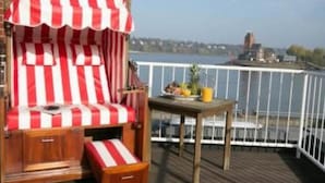 A deck with a red and white striped chair and a small table with fruits and a drink. - Hotel AM ELBUFER (Hamburg)