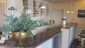 A modern kitchen with a marble countertop, a large potted plant, and a bar area with a white sink and bar stools. - Hotel AM ELBUFER (Hamburg)