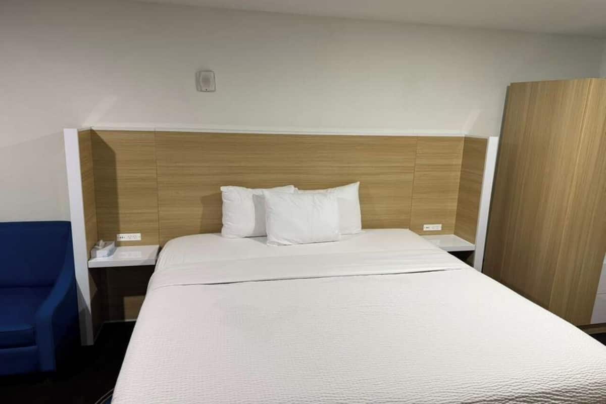 A hotel room with a bed, a nightstand, a blue chair, and a wardrobe.