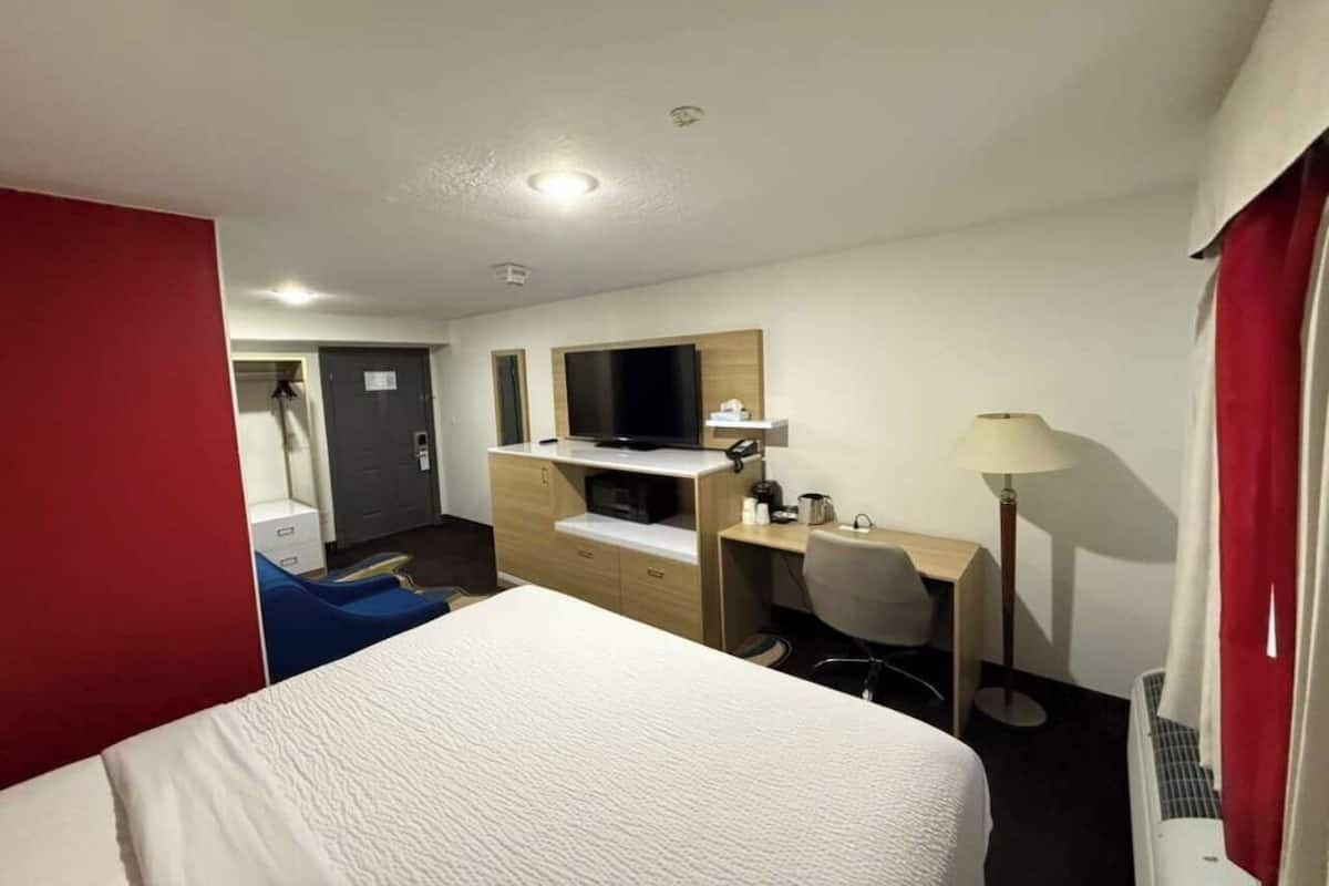 A hotel room with a bed, a desk, a TV, and a chair.