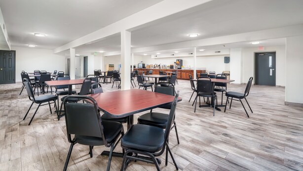 A spacious indoor area with multiple tables and chairs, a kitchen area in the background, and a wooden floor.