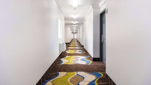 A long, narrow hallway with a patterned carpet, white walls, and a series of doors on one side.