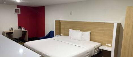 A hotel room with a bed, a desk, a chair, and a red accent wall.