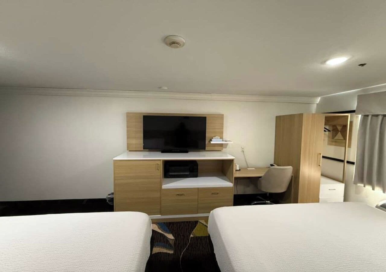 A hotel room with two beds, a TV on a wooden stand, a desk, and a wardrobe.