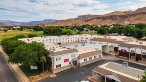 A large, multi-story building with a flat roof and several air conditioning units. There is a sign for 'Ramada' on the building, and a parking lot in front.