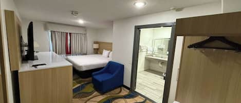 Habitación de hotel con cama, escritorio, silla, baño y vista a la ciudad.