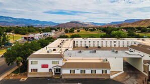 A motel with a parking lot, a gas station, and mountains in the background.