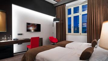 A modern hotel room with a brick-patterned ceiling, a large bed with white linens, a desk with a red chair, and a television mounted on the wall.