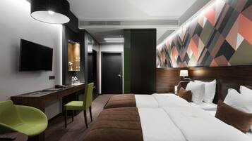 Habitación de hotel con una cama grande, un escritorio con silla, televisor y una pared con diseño geométrico.