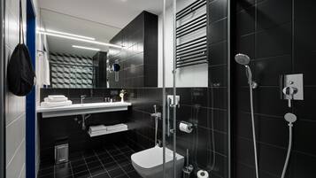 A modern bathroom with a glass-enclosed shower, a white toilet, and a sink with a towel rack.