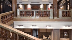 Una imponente escalera con barandales ornamentados, un candelabro y columnas clásicas en un amplio vestíbulo.