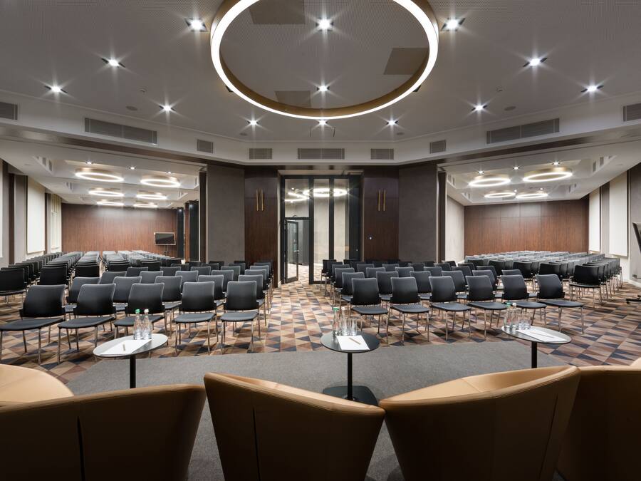 A conference room with rows of chairs, tables, and a circular light fixture on the ceiling.