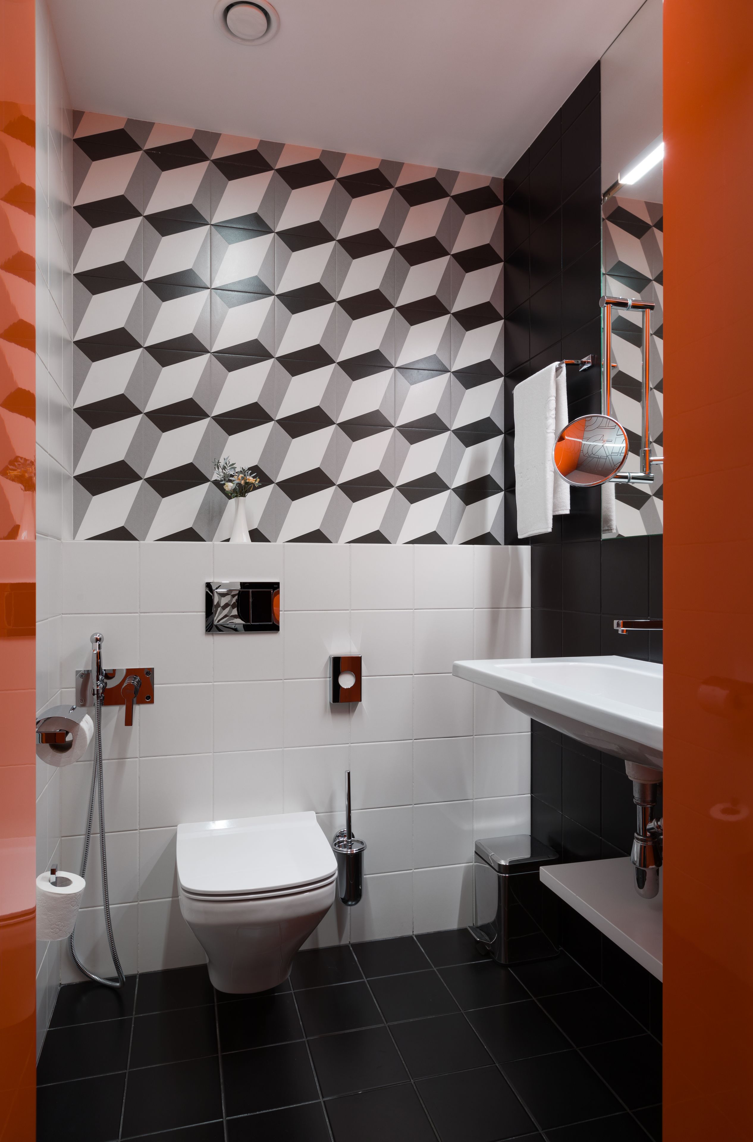 A modern bathroom with a geometric patterned wall, a white toilet, a sink with a mirror, and a shower area.
