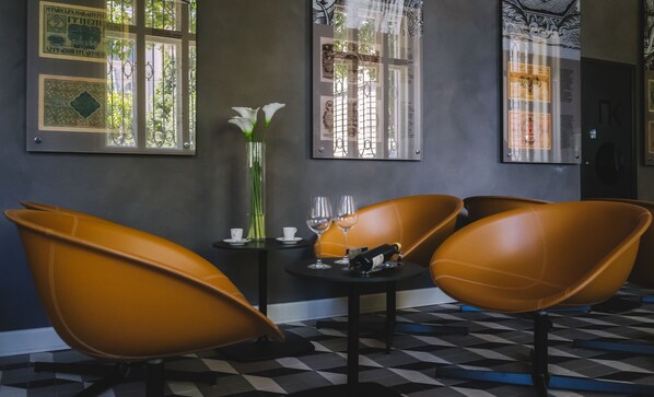Un área de comedor con piso a cuadros, una mesa con copas de vino, un florero con flores y dos sillas marrones.
