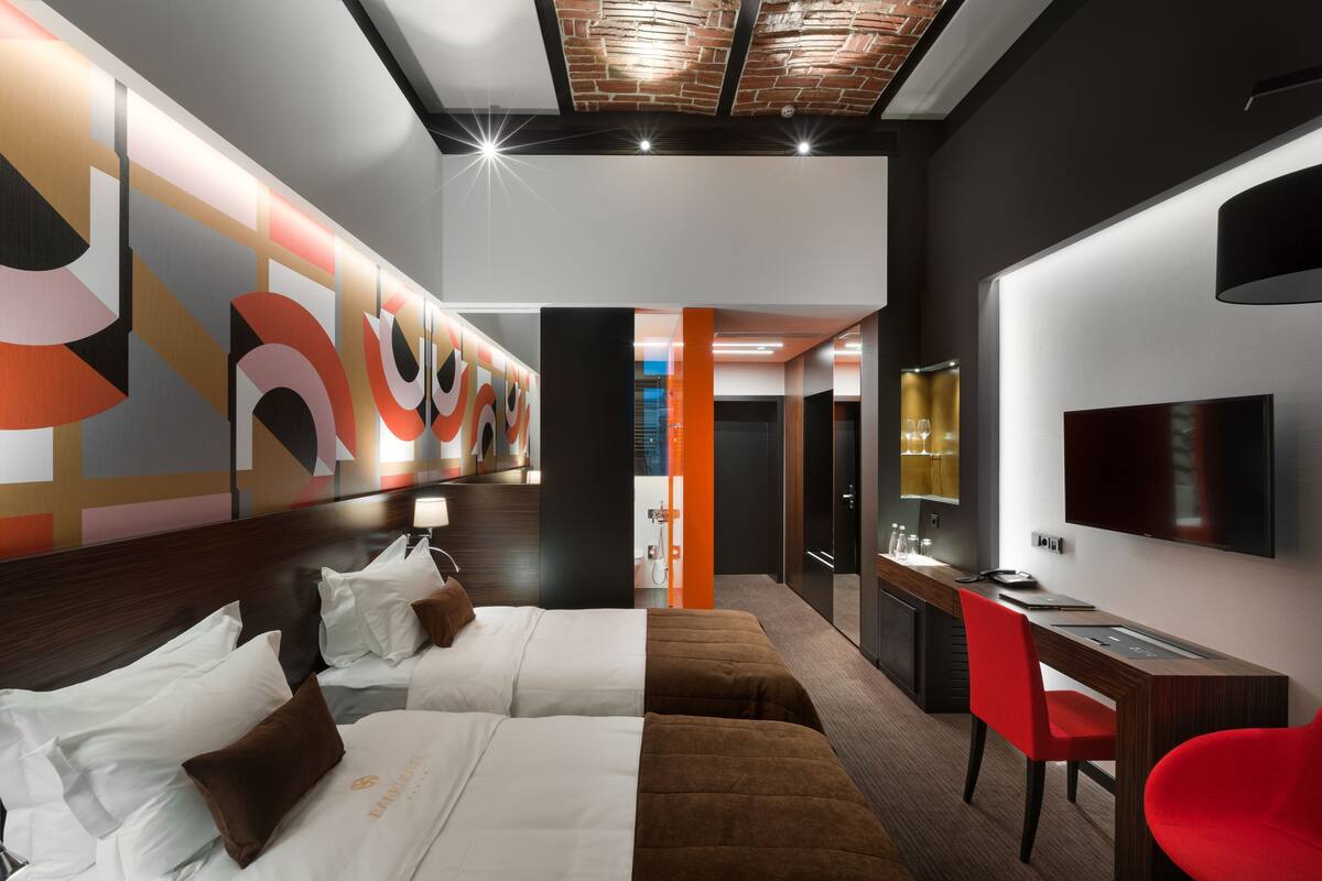 A hotel room with a modern design, featuring a large bed, a desk, and a TV.