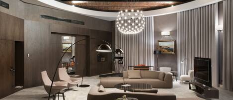 A modern living room with a curved ceiling, a large chandelier, a flat-screen TV, and a round coffee table.
