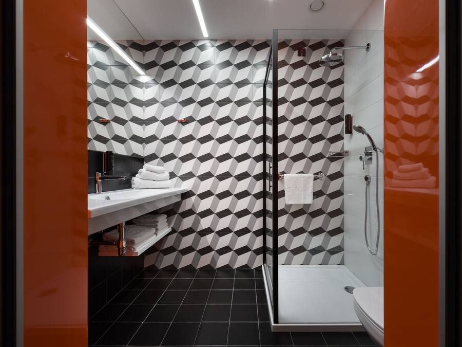 A modern bathroom with a geometric patterned wall, a glass shower enclosure, and a white sink with a towel rack.