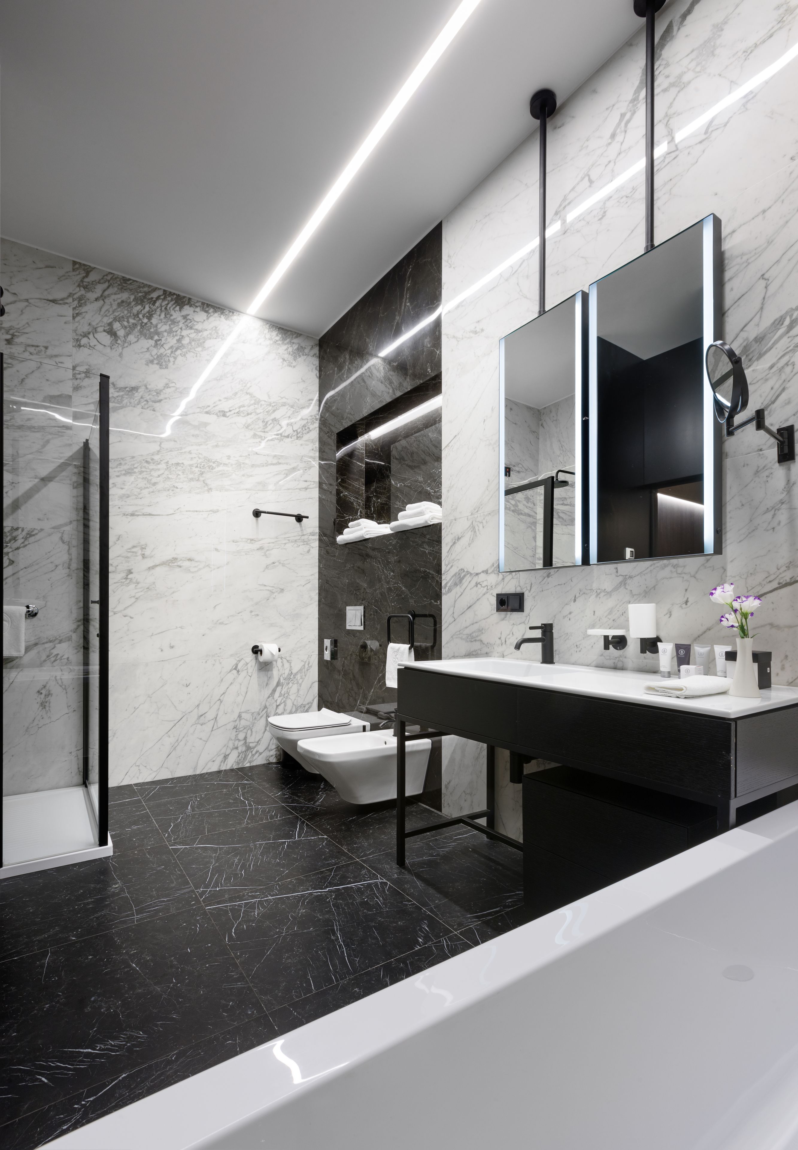 A modern bathroom with a marble wall, a black floor, a white sink, and a large mirror.