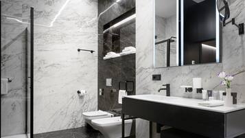 A modern bathroom with a marble wall, a black floor, a white sink, and a large mirror.