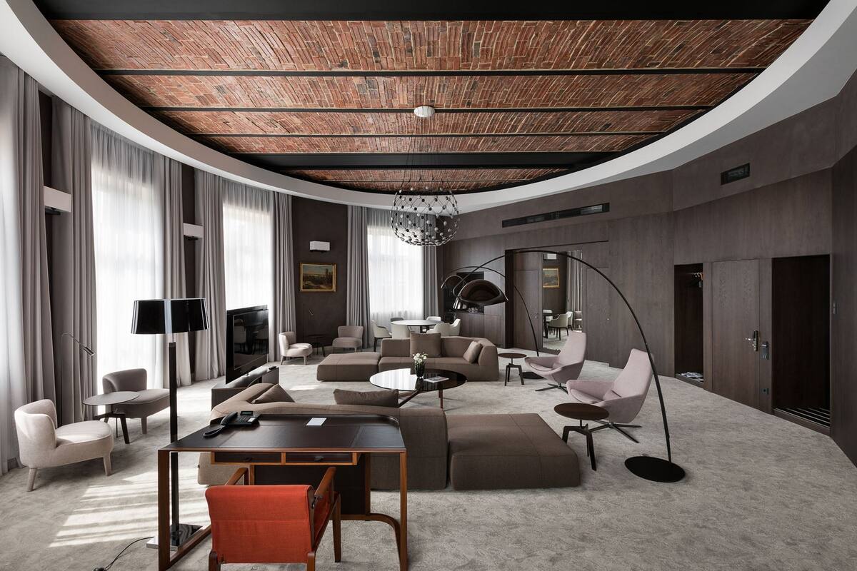 A modern living room with a curved ceiling, large windows, and a mix of seating areas including sofas and chairs.