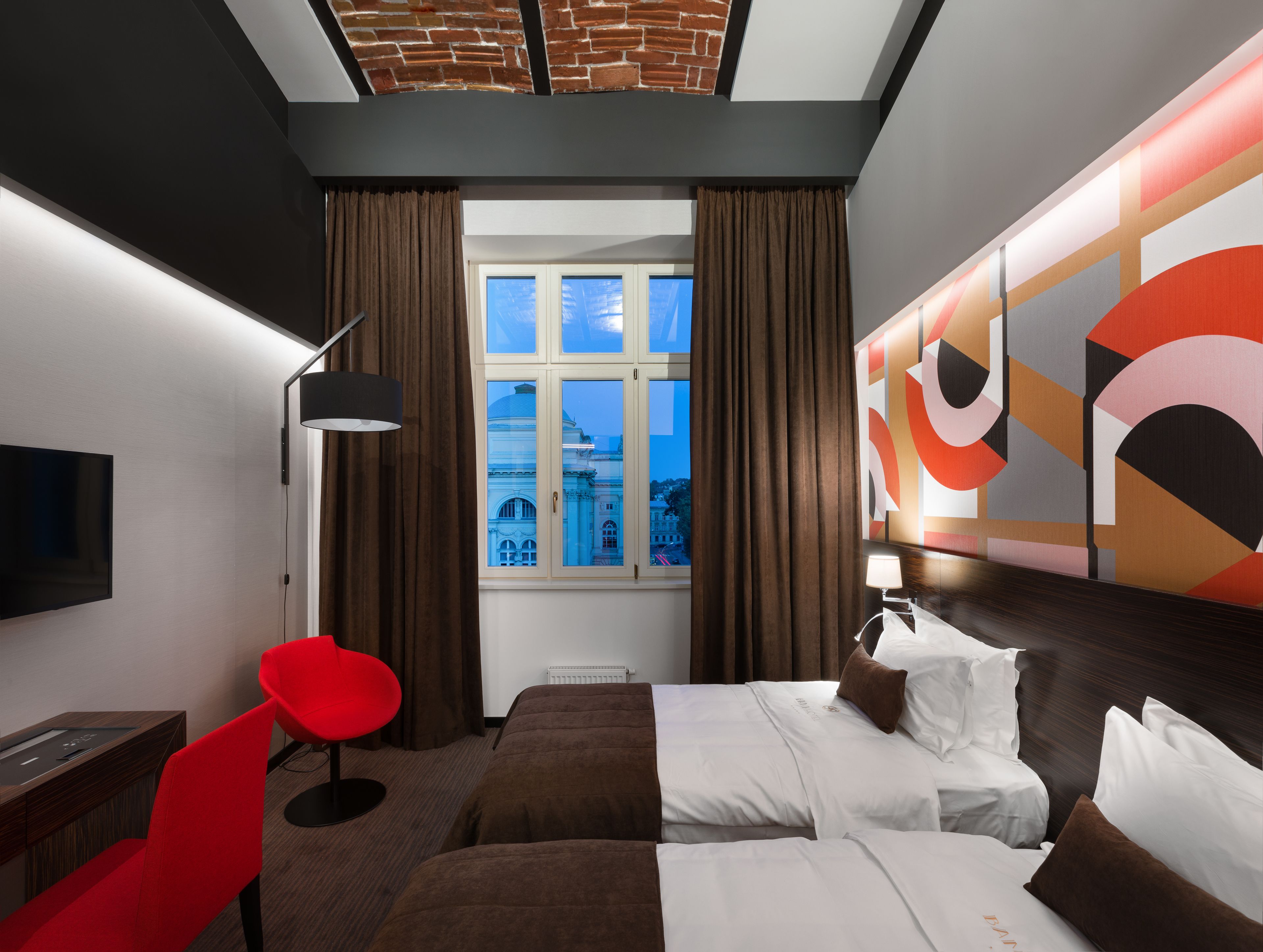 Habitación de hotel con una cama grande, una silla roja, un escritorio, un televisor y una ventana con vistas a un edificio.