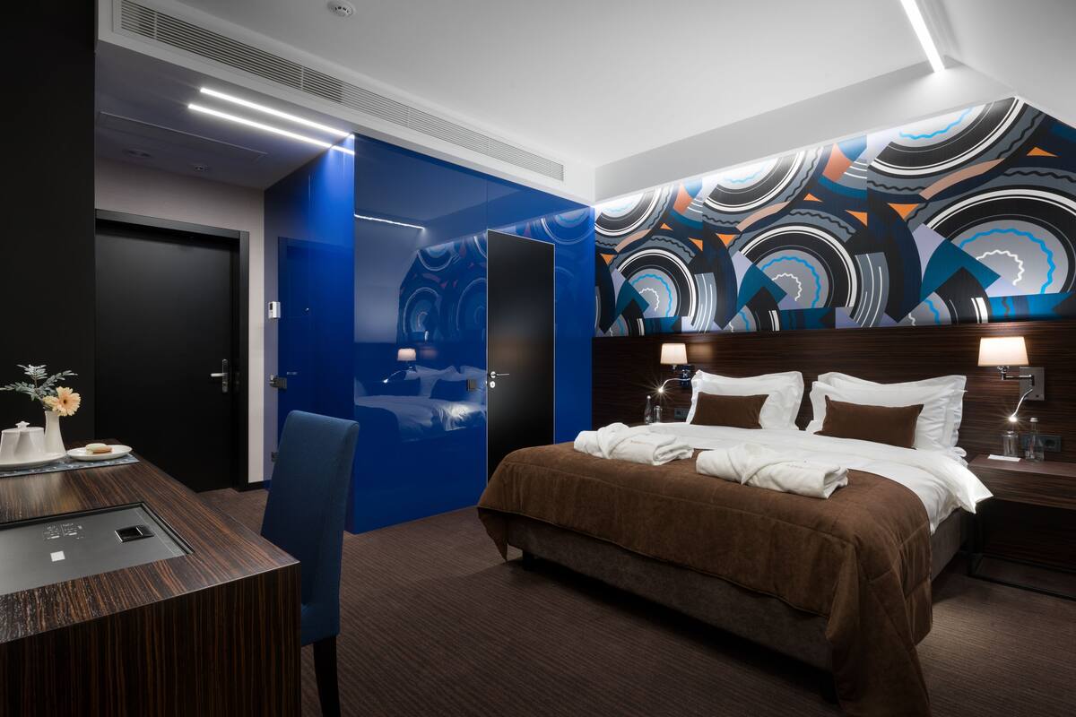 A modern hotel room with a large bed, a desk, and a blue accent wall.