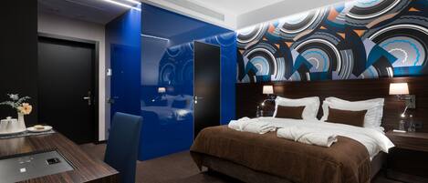 A modern hotel room with a large bed, a desk, and a blue accent wall.