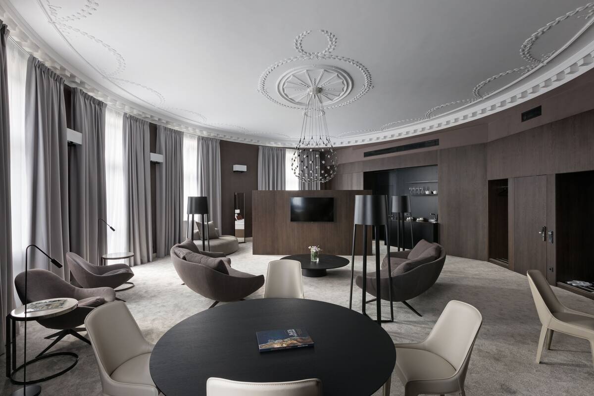 A modern hotel room with a round table, comfortable seating, a flat-screen TV, and a decorative ceiling.