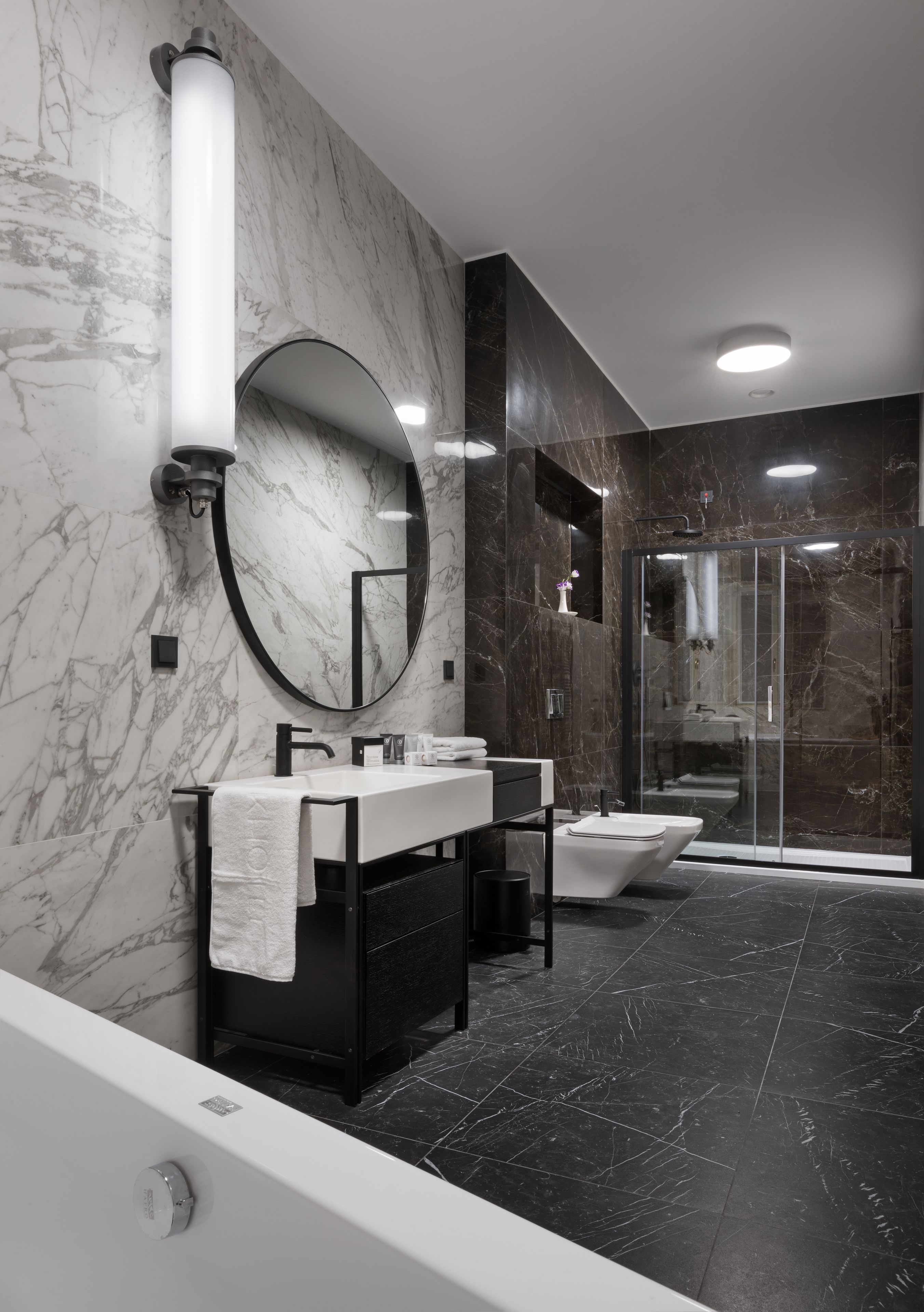 Un baño moderno con pared de mármol, un espejo grande, una bañera y una ducha con mampara de vidrio.
