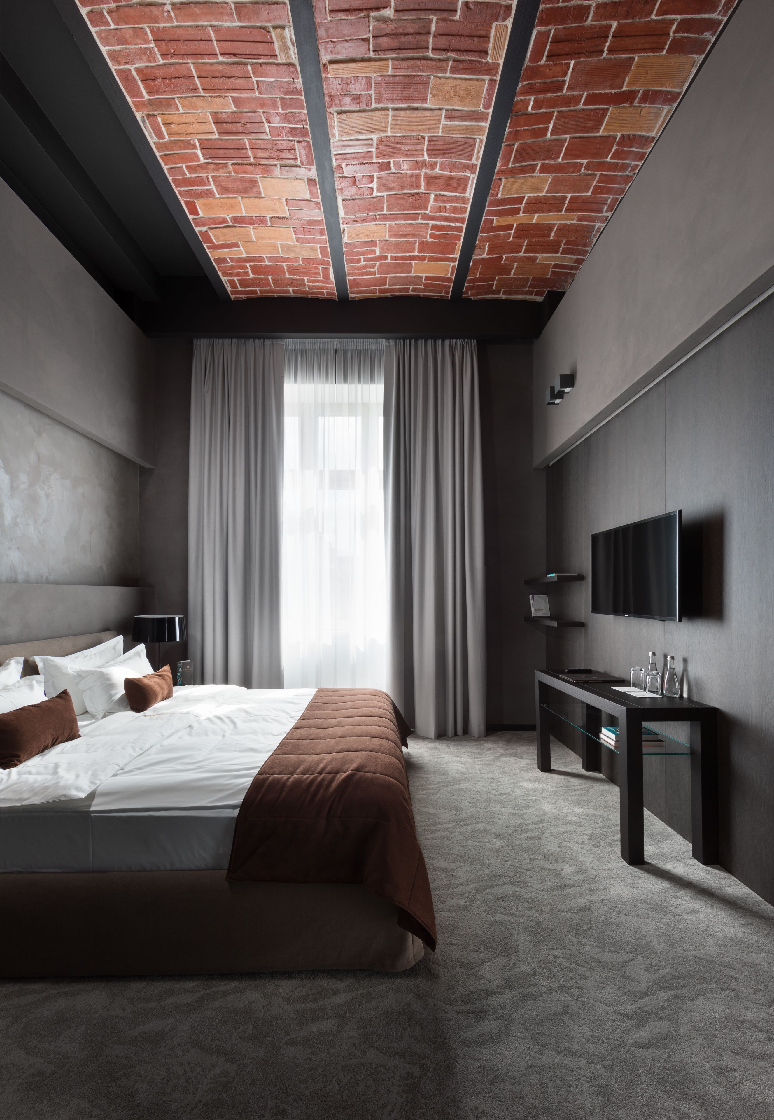 A modern bedroom with a brick ceiling, a large bed, a TV, and a desk.