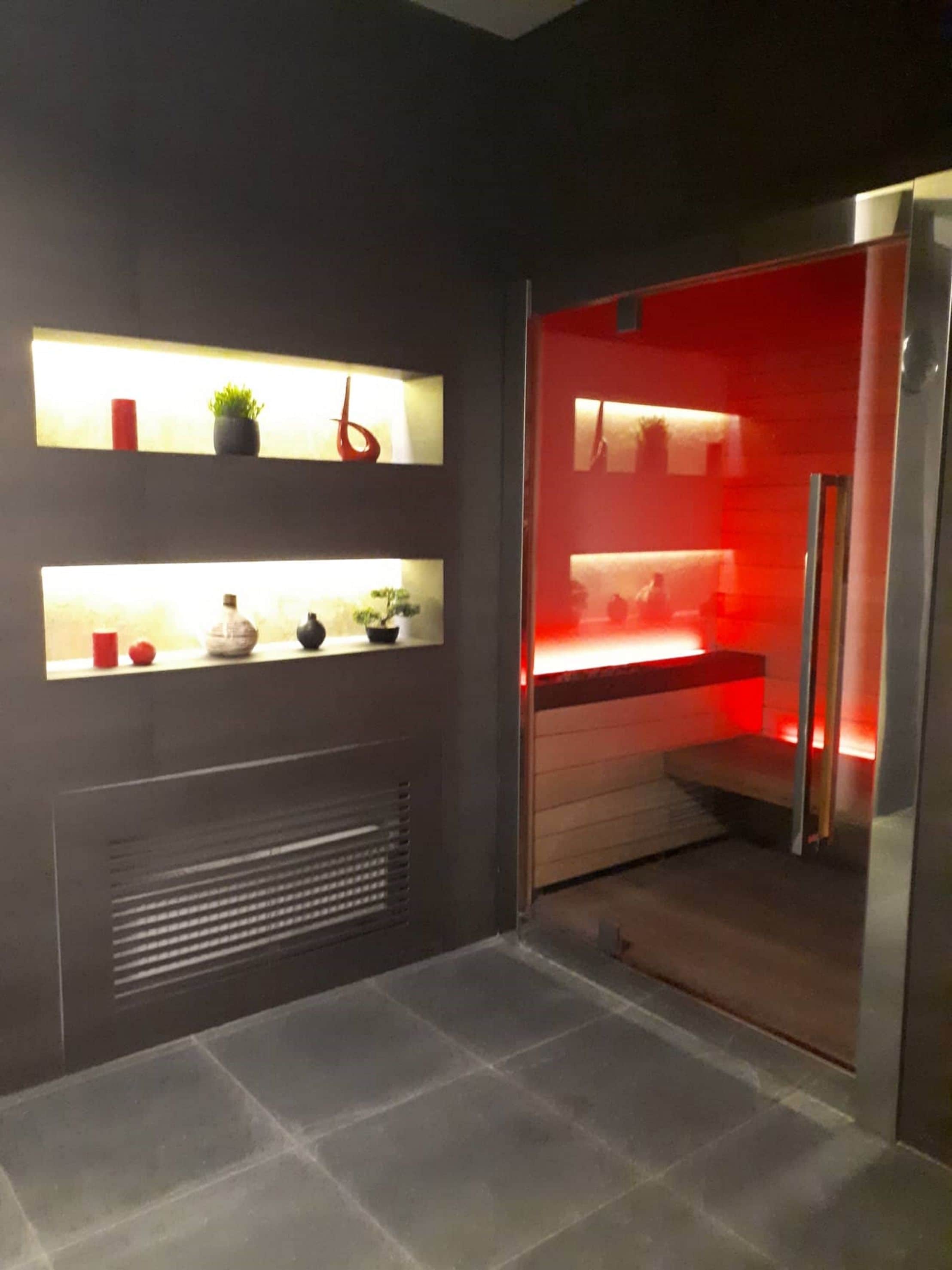 A modern bathroom with a dark tiled floor, a built-in shower with a red light, and shelves with decorative items.