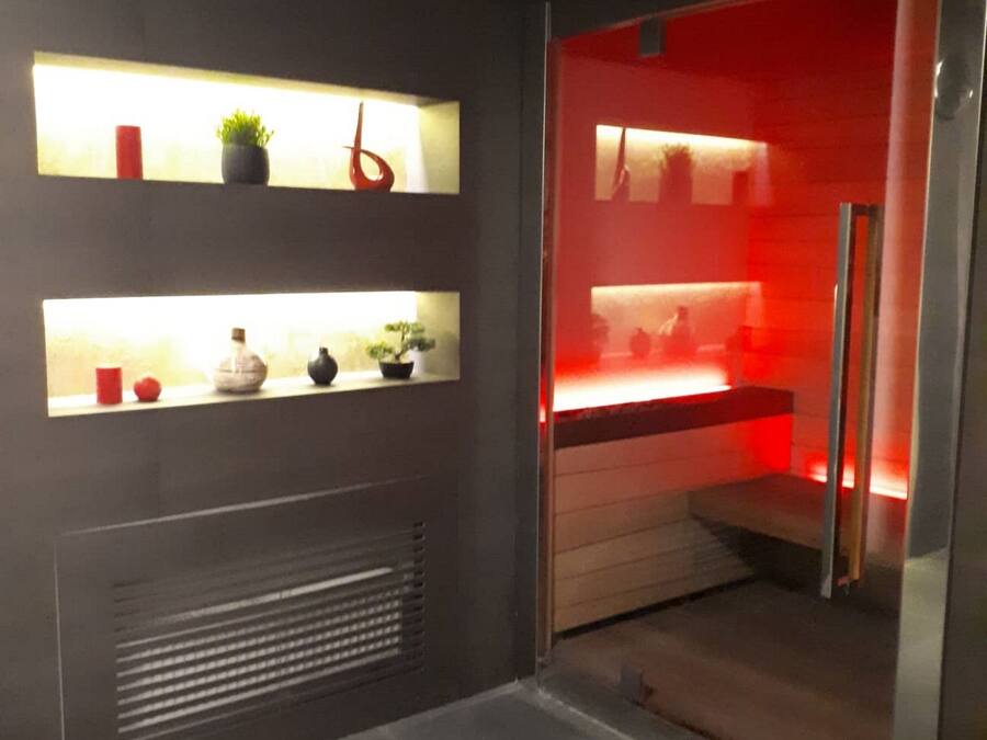 A modern bathroom with a dark tiled floor, a built-in shower with a red light, and shelves with decorative items.
