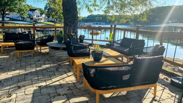An outdoor seating area with wicker furniture and potted plants, overlooking a body of water. - Buddy's Harbor (Lake Ozark)