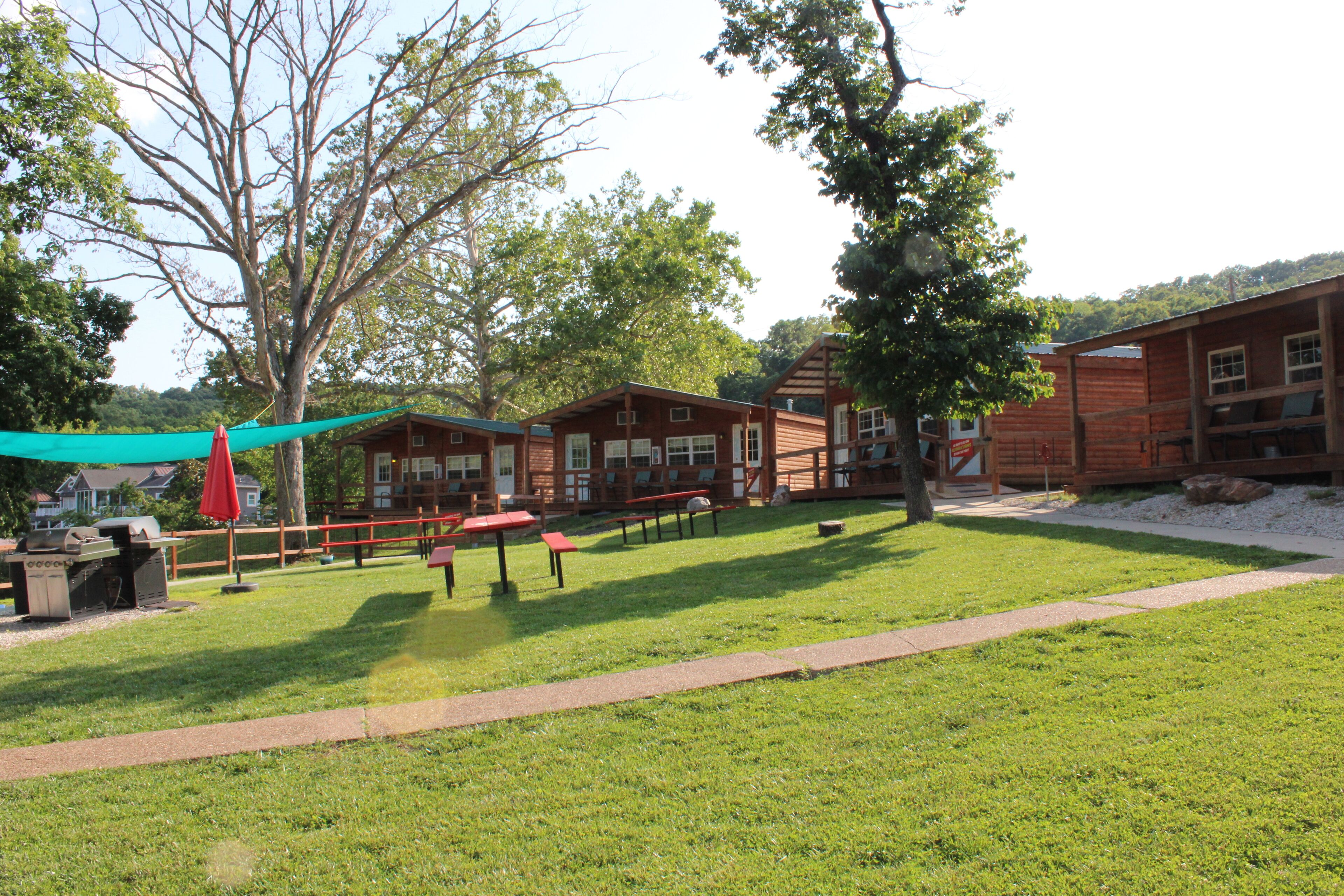 A grassy outdoor area with picnic tables and a barbecue grill.