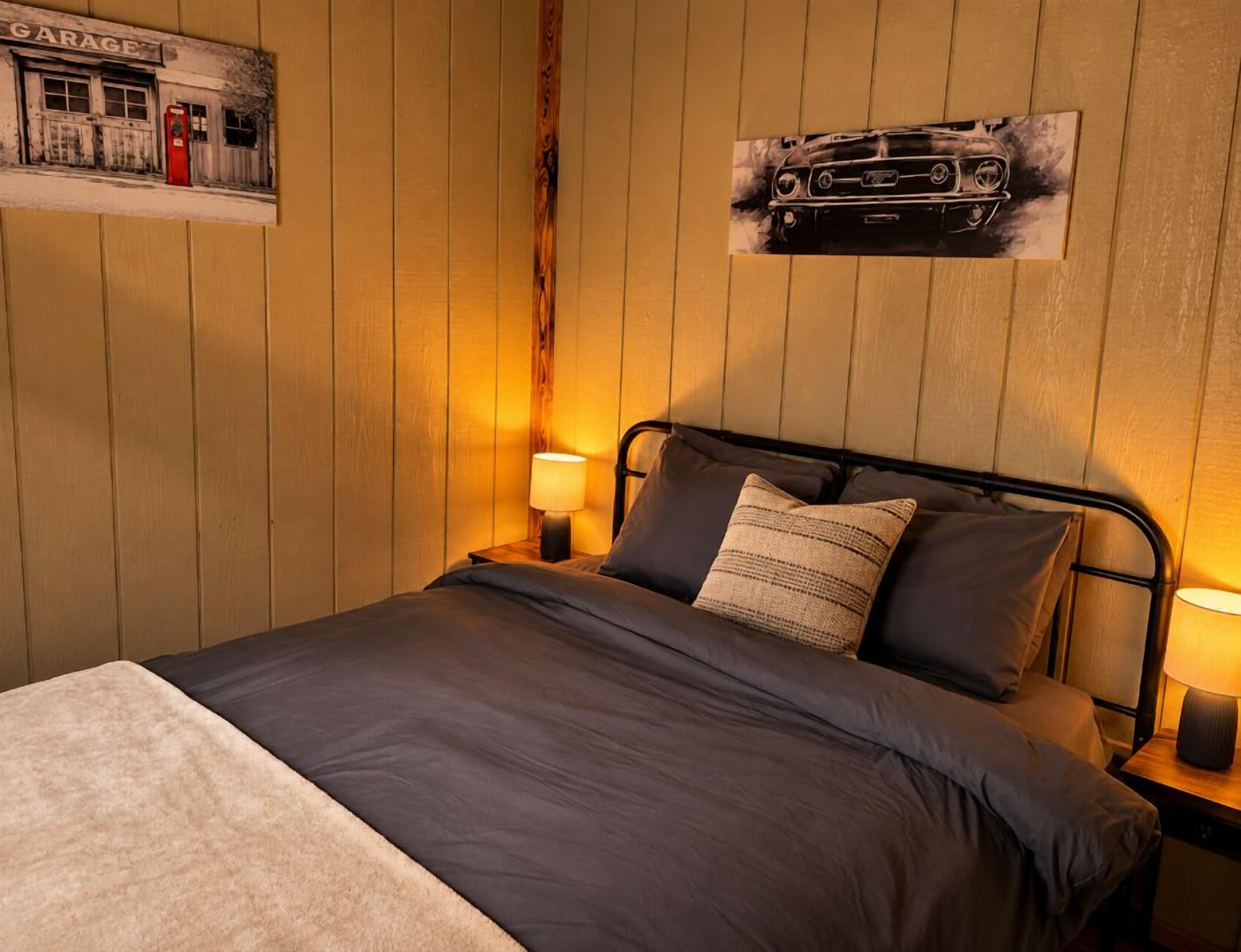 Una camera da letto con un letto, due abat-jour, un poster di un'auto appeso al muro e pannelli in legno a rivestimento.