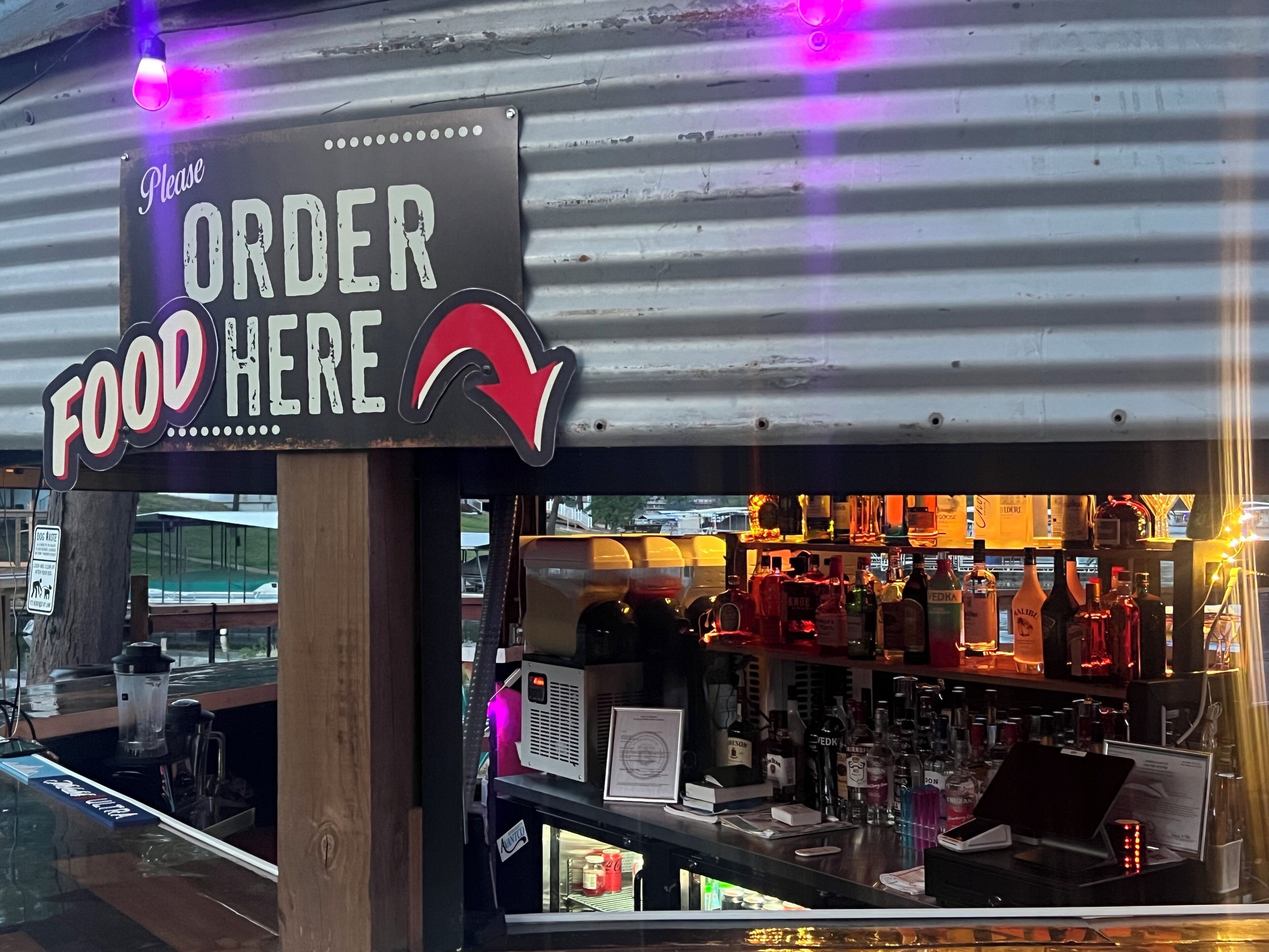 A restaurant with a sign that says "Please ORDER HERE" and a bar area visible through the window.