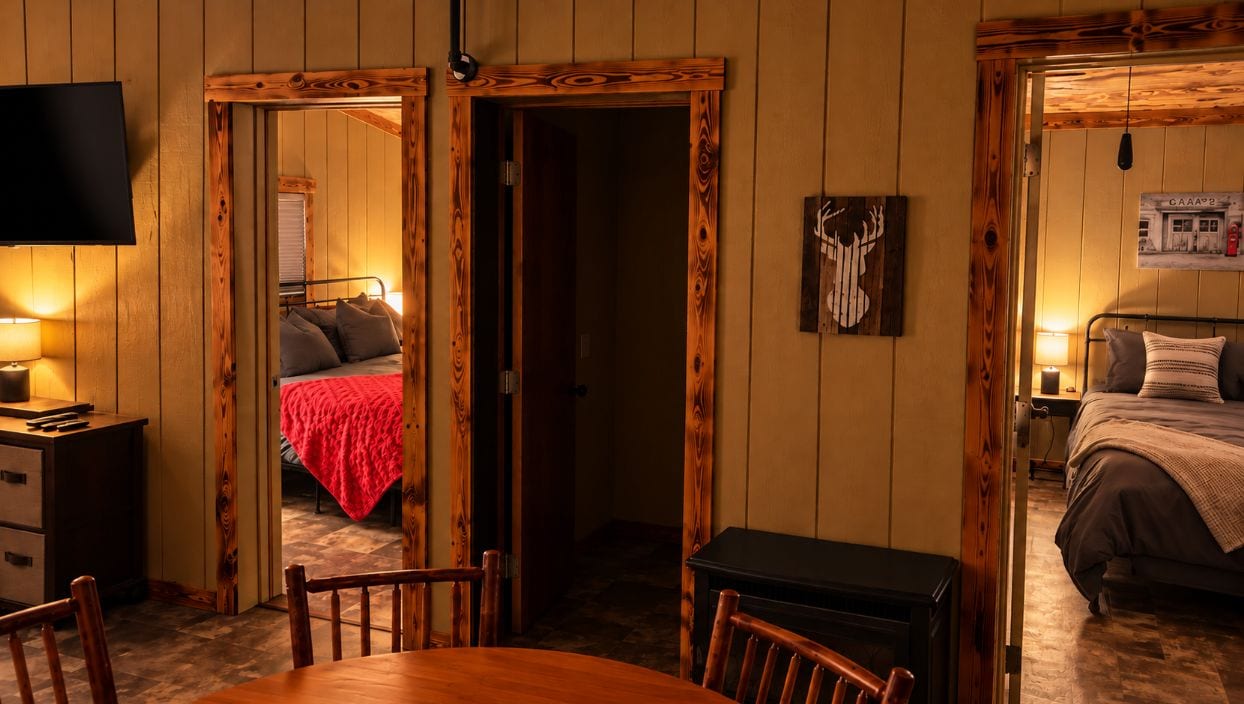 Ein Zimmer mit Holzboden, einem Bett mit roter Decke, einem Schreibtisch mit Lampe und einem an der Wand montierten Fernseher.