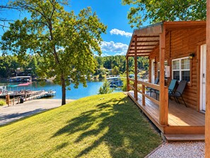 A wooden cabin with a porch overlooking a lake, dock, and boats. - Buddy's Harbor (Lake Ozark)