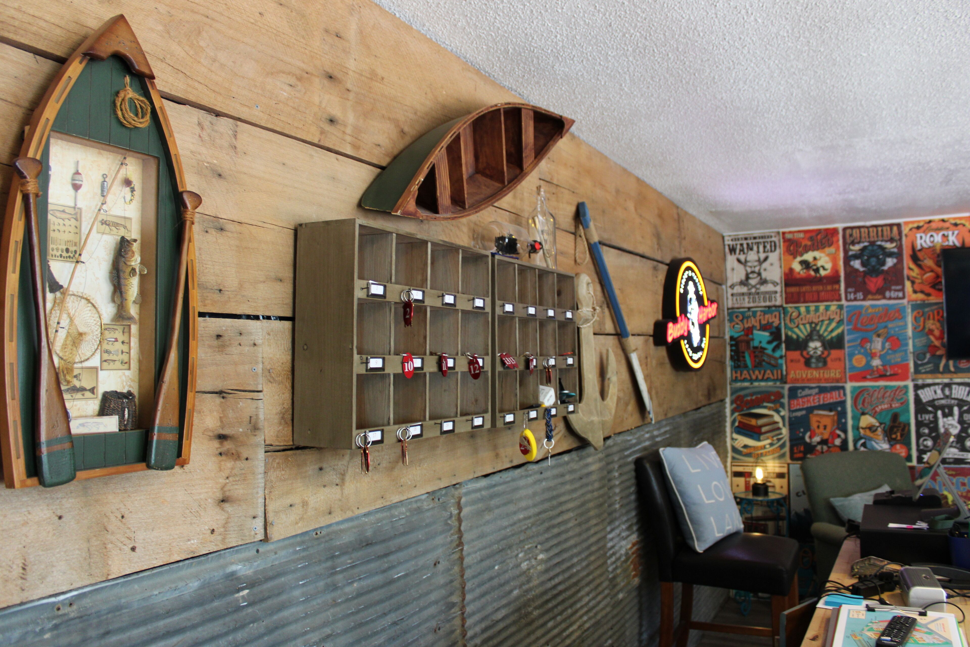 Um quarto com parede de madeira, um painel perfurado com chaves, um letreiro de neon e diversos cartazes.