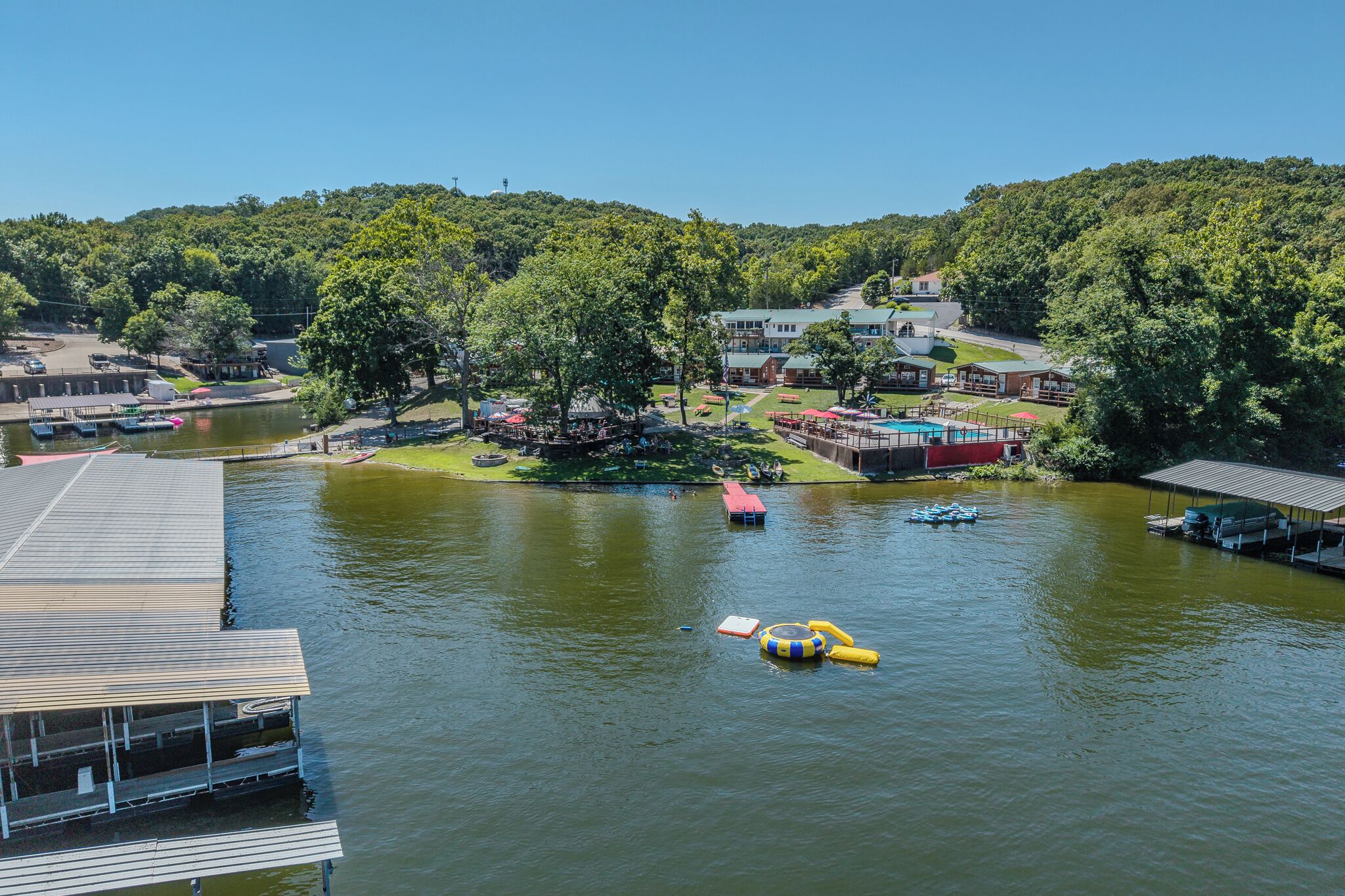 A lakeside resort with a dock, boats, and a covered seating area.