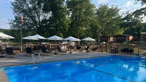 A swimming pool with lounge chairs and umbrellas, surrounded by trees and a wooden deck. - Buddy's Harbor (Lake Ozark)
