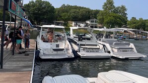 A marina with several boats docked, a covered area with people, and a clear sky. - Buddy's Harbor (Lake Ozark)
