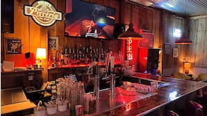 A bar area with a wooden interior, a TV screen, and various bottles and glasses on the counter. - Buddy's Harbor (Lake Ozark)
