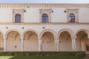 A building with a series of arches and columns, a tiled roof, and a well-maintained lawn. - B&B Foresteria dell'Abbazia (Montescaglioso)