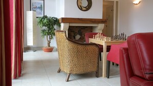 Un salon avec une cheminée, une table d’échecs, un fauteuil en osier et un canapé rouge.